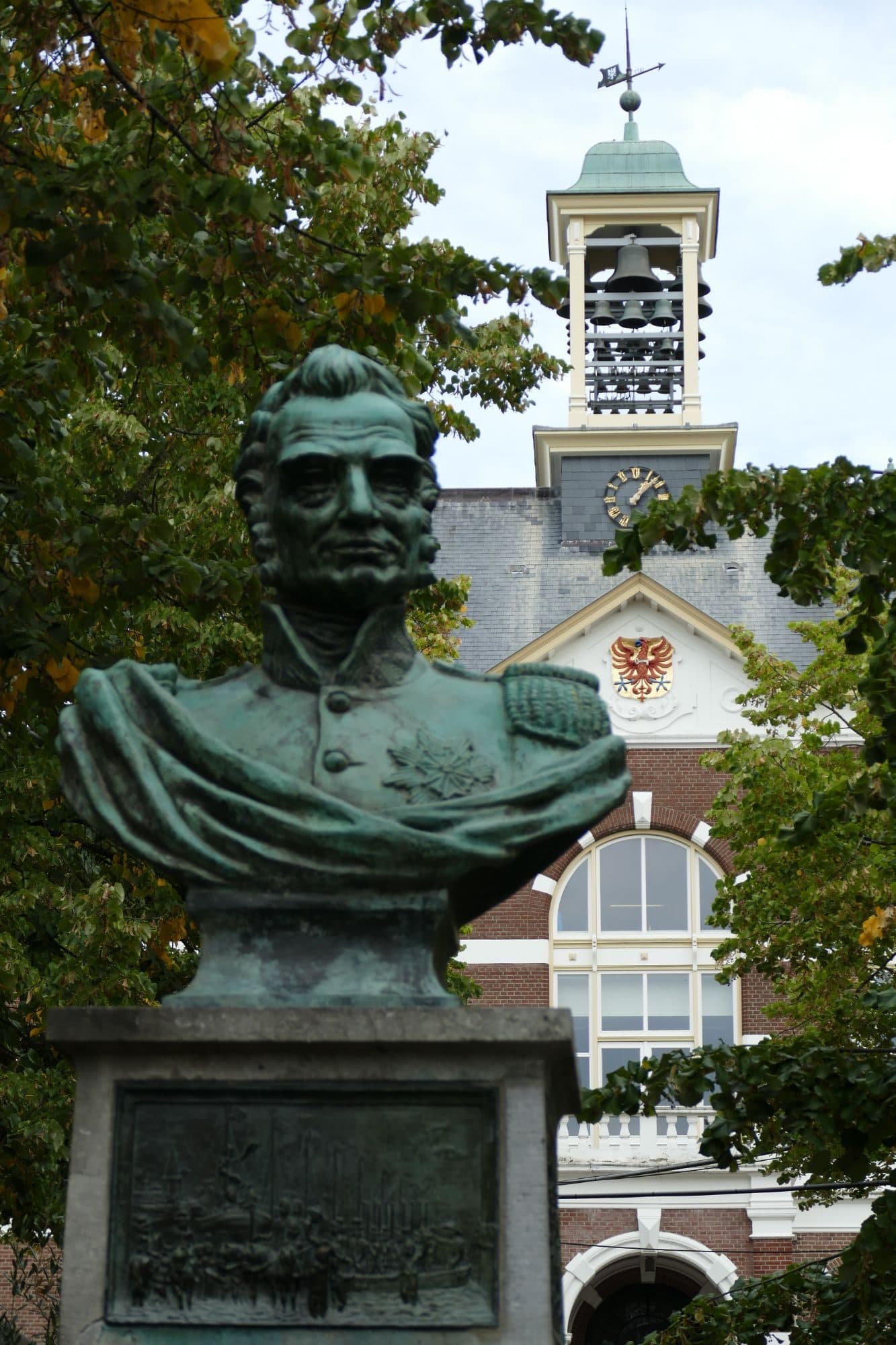 Bronzen borstbeeld van koning Willem I op het Raadhuisplein in Apeldoorn, met de toren van het raadhuis erachter
